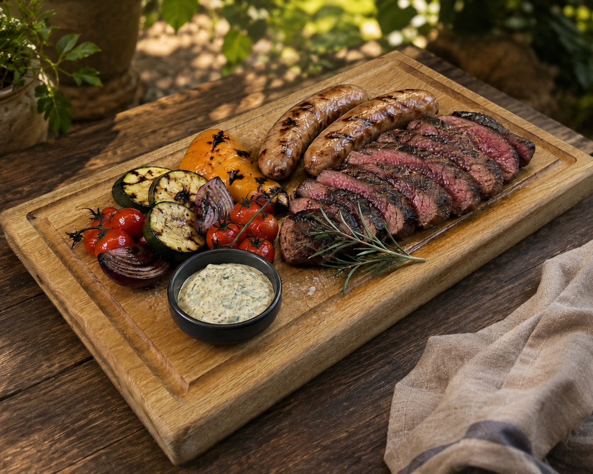 BBQ-Platte für sechs Personen mit aufgeschnittenem Steak, Salsiccia, Grillgemüse und Kräuterdip auf großem Eichenbrett