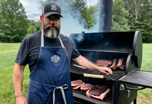 Bärtiger Mann in einer Schürze, der Fleisch grillt.