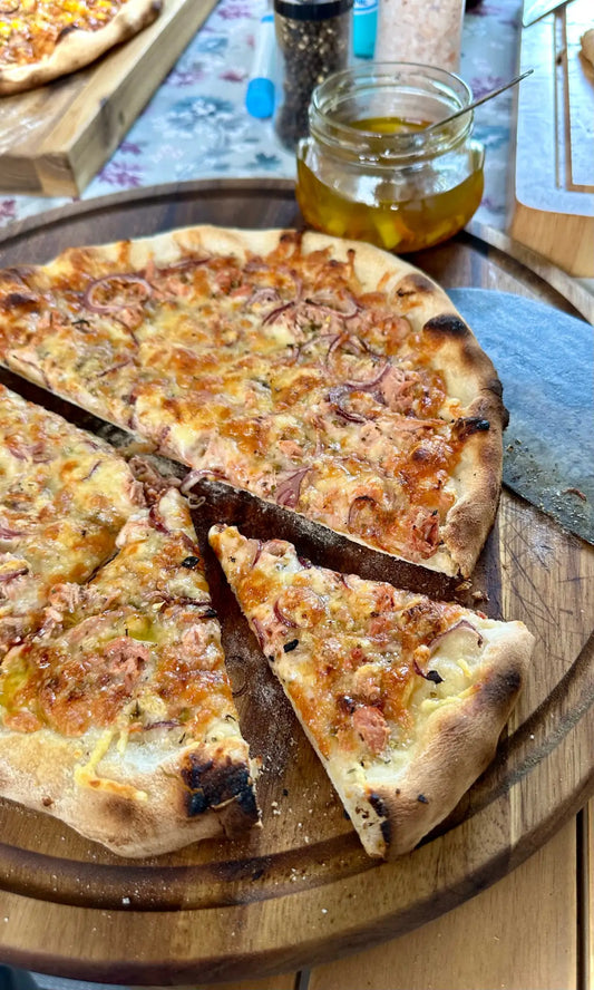 Mit karamellisierten Zwiebeln und geschmolzenem Käse belegte Pizza auf einem Holzschneidebrett.