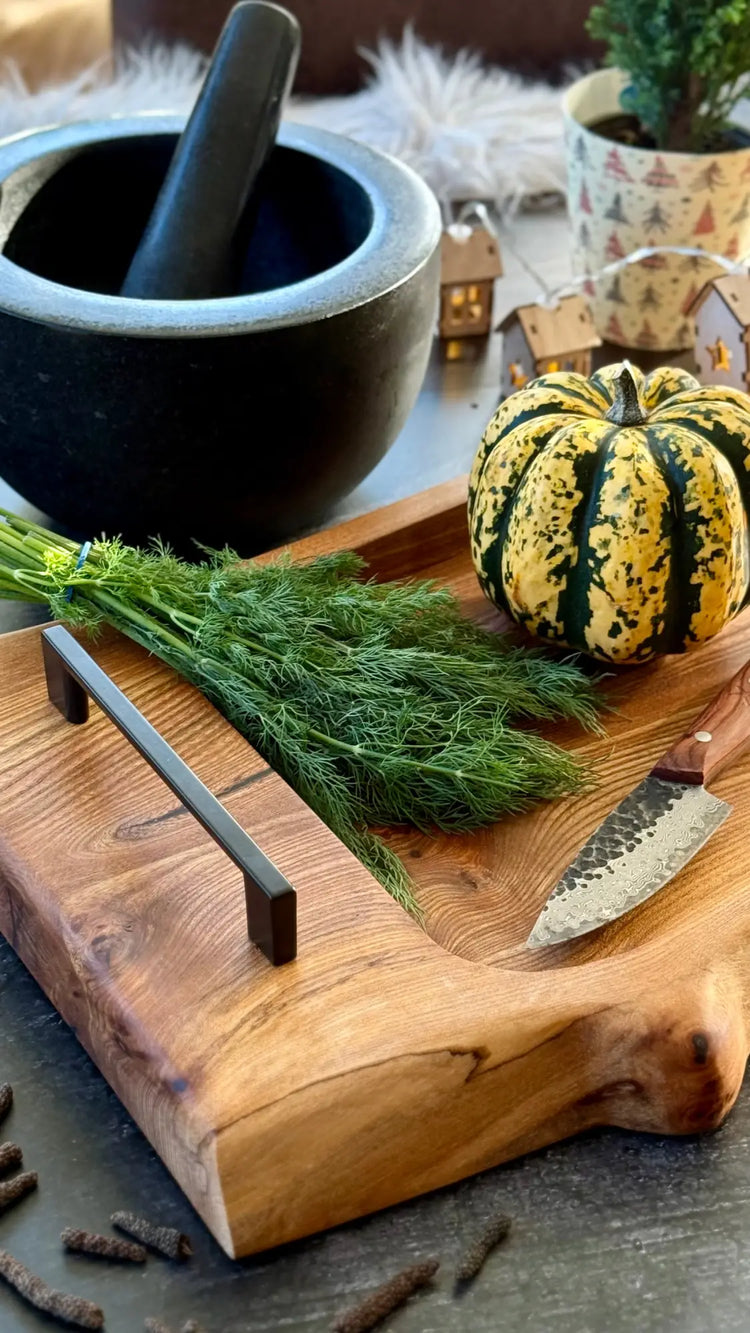 Rustikales Holzschneidebrett mit frischem Dill, einem dekorativen gestreiften Kürbis und einem schwarzen Mörser und Stößel.