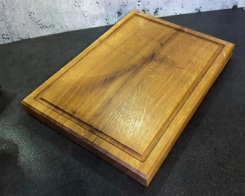 Massives Eichen-Schneidebrett 40×30 cm mit Saftrille auf einer Kücheinrichtung, dekoriert mit frischem Gemüse und Kräutern.