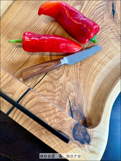 Zwei rote Paprika auf einem handgefertigten Eschenholz Servierbrett mit Messer