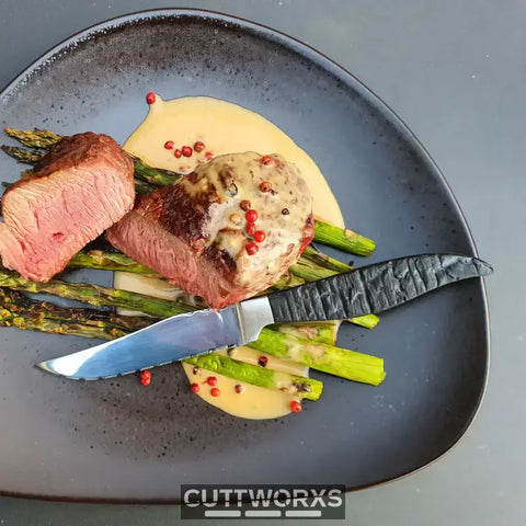 Steak à cuisson à point avec des asperges et une sauce crémeuse sur une assiette sombre, idéal pour un bon couteau à steak.