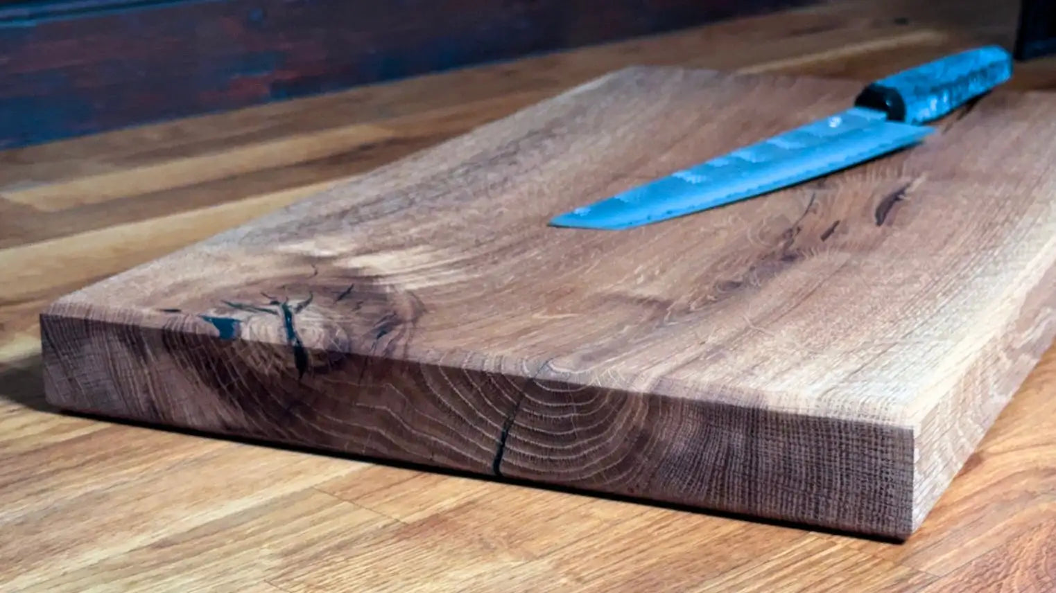 Ein rustikales, dunkelbraunes Holzschneidebrett mit sichtbarer Maserung und natürlicher Kante.