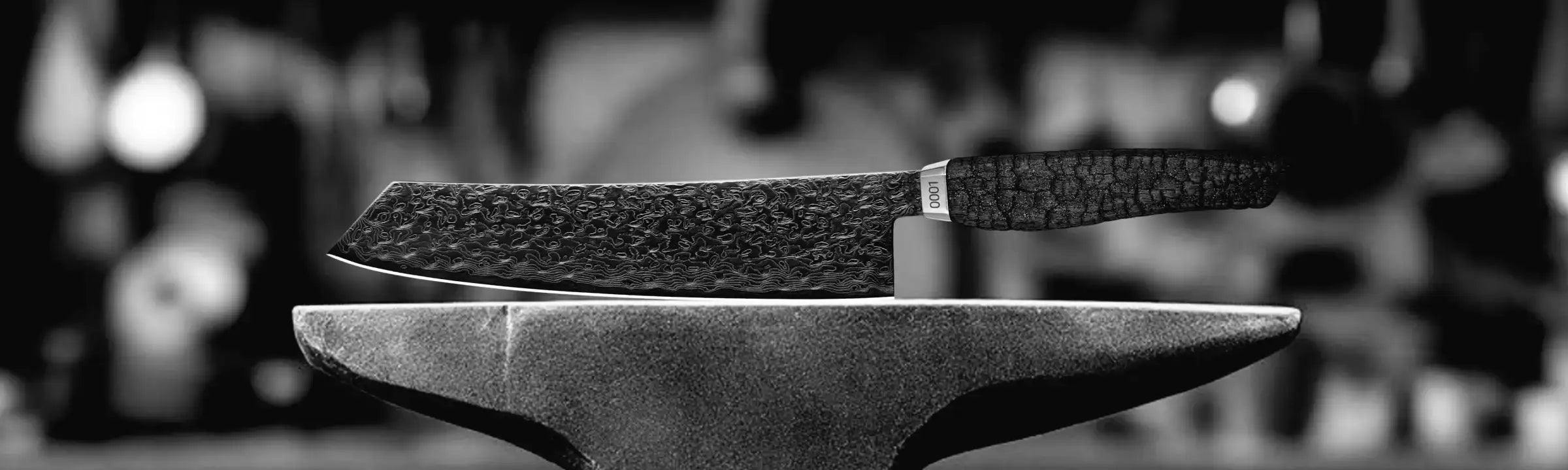 Schwarzes texturiertes Messer mit einer gehämmerten Klinge, das auf einem Amboss ruht.