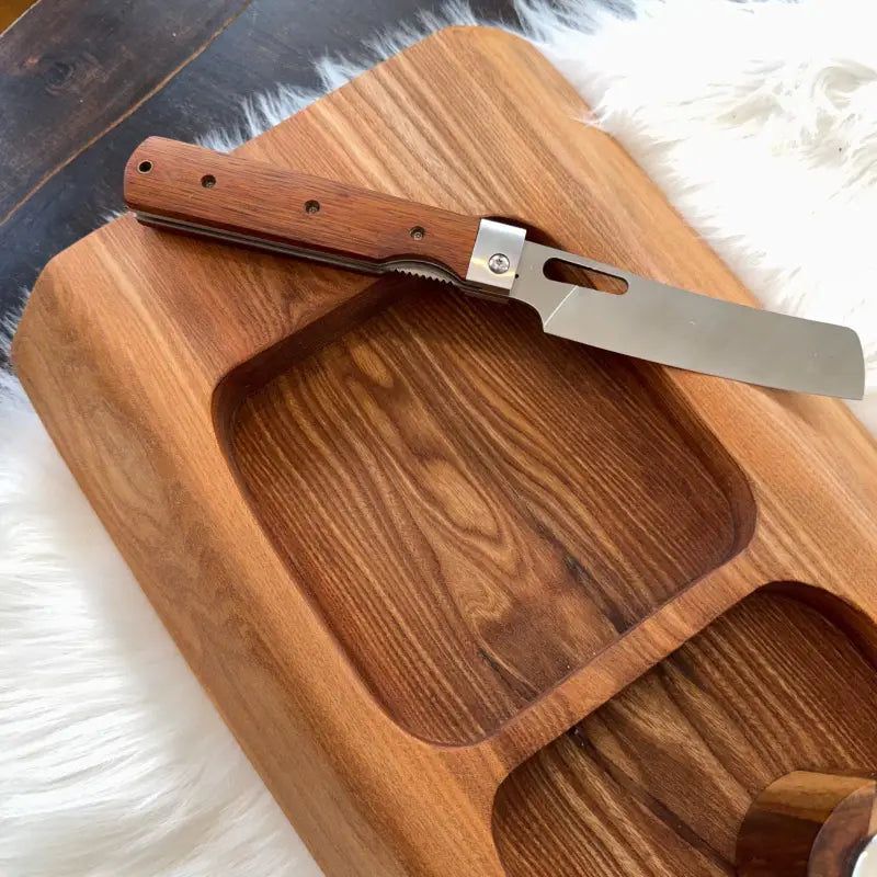 Holzbrett mit Ausfräsungen und Klappmesser auf handgefertigtem Snackboard aus Ulmenholz